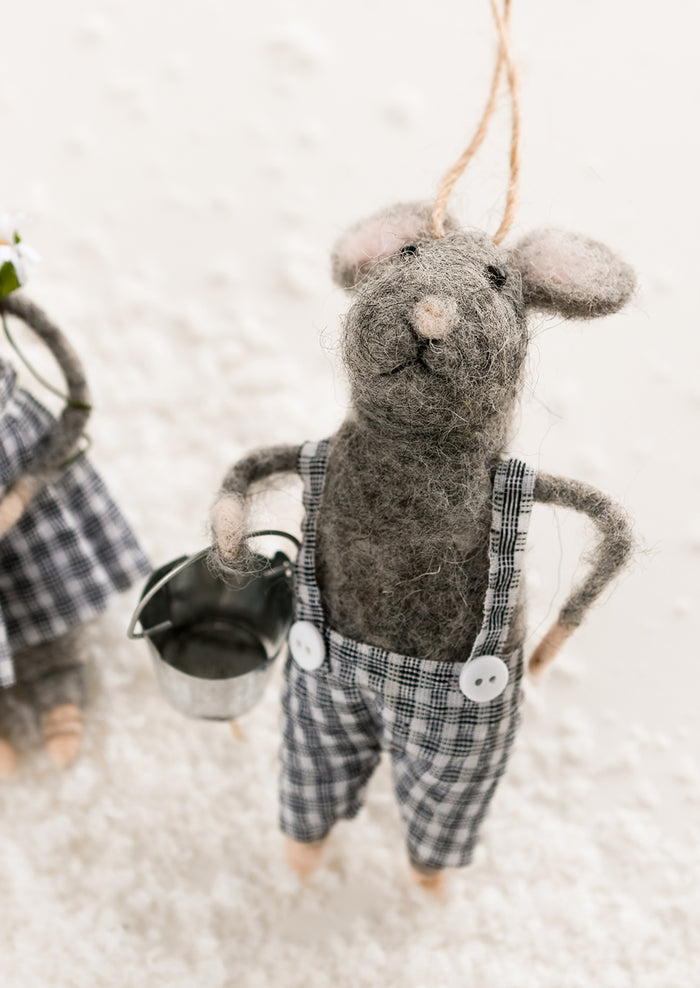 A felted grey mouse ornament in gingham suspenders, holding metal bucket.