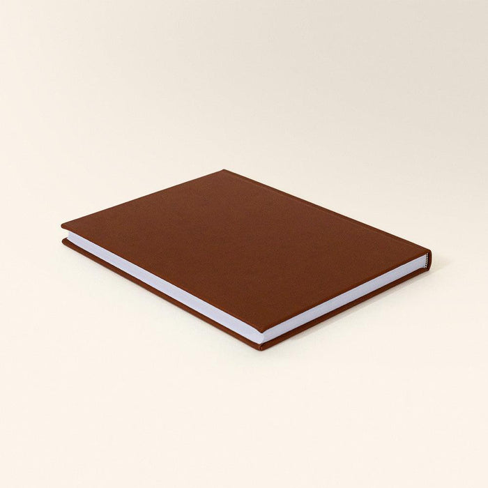 Closed large sketchbook with a chestnut brown cover angled on a white background