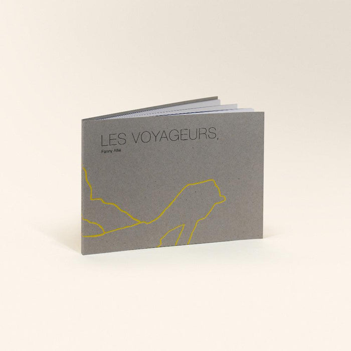 Gray zine titled Les Voyageurs with a yellow abstract drawing standing slightly ajar showing pages