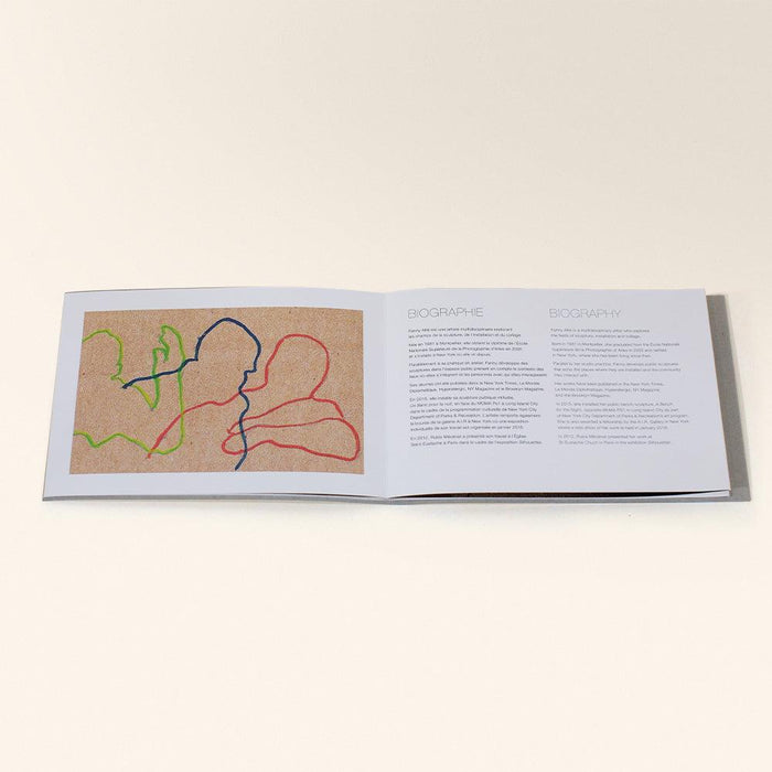 An open book titled Les Voyageurs with abstract line drawings in red blue and green on a brown page