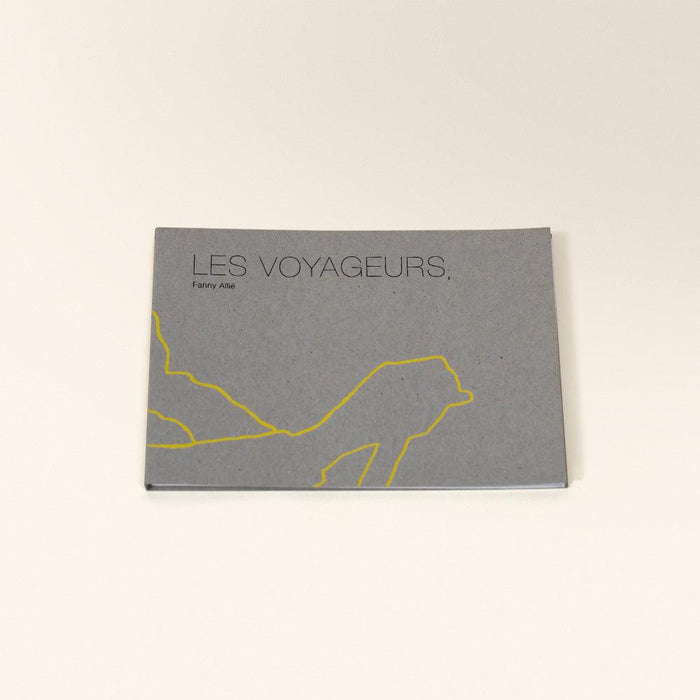 Gray zine with Les Voyageurs title and a yellow outline drawing of a person walking across the bottom
