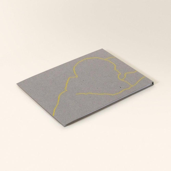 Back of a gray zine with a yellow abstract outline of a figure or landscape lying flat