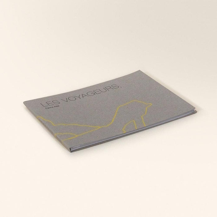 Gray zine titled Les Voyageurs with a yellow outline drawing of a person walking viewed from an angle