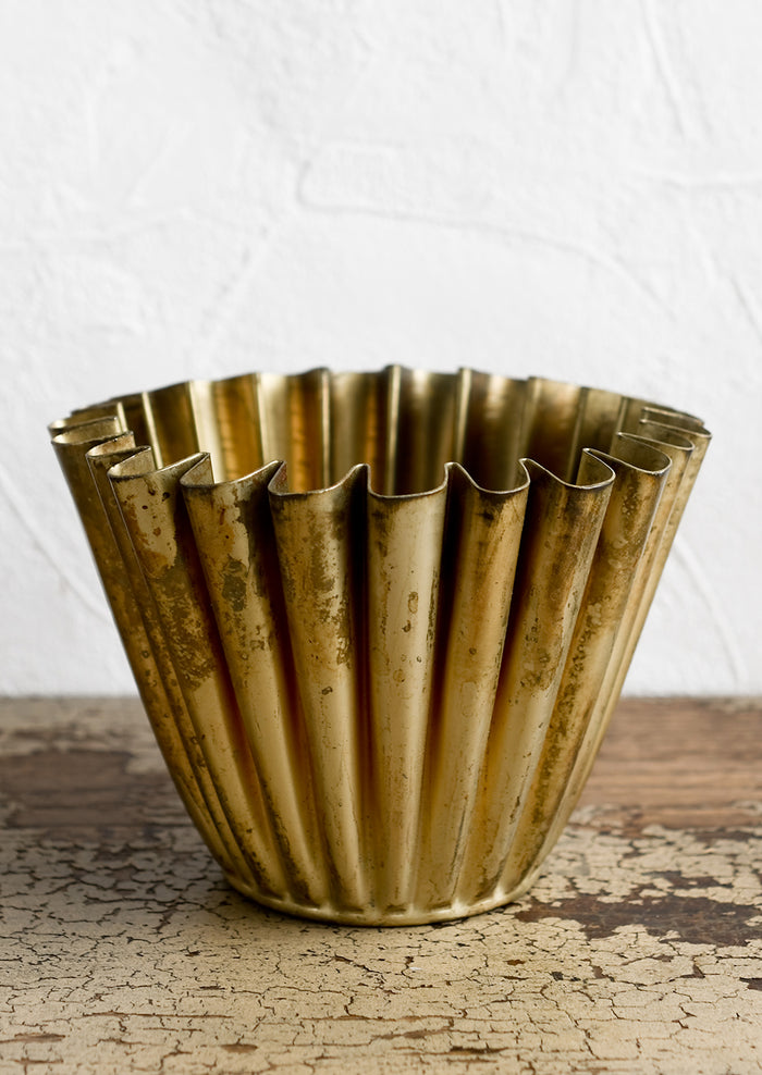 A pleated metal planter in distressed brass finish.