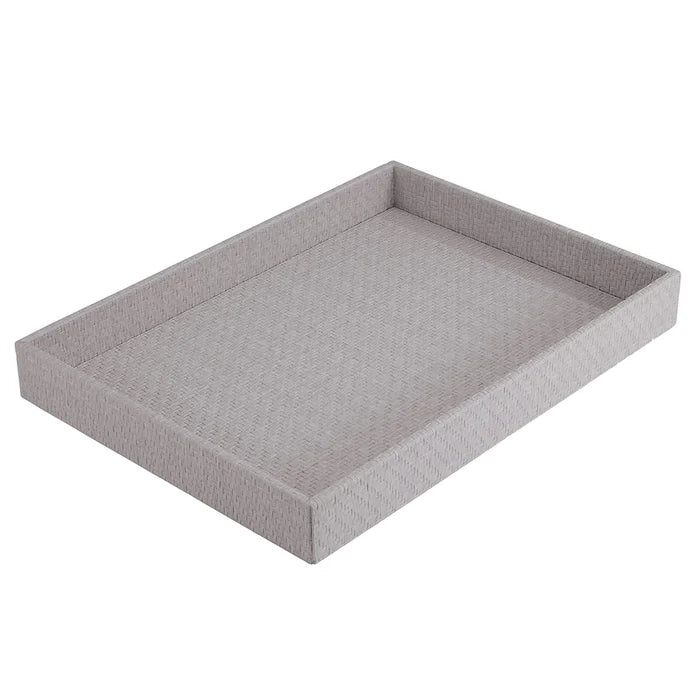 The Bodrum Wicker Rectangle Tray Grey is a light gray woven tray with raised edges and a textured design, shown angled against a white background. This serving tray has no visible handles.