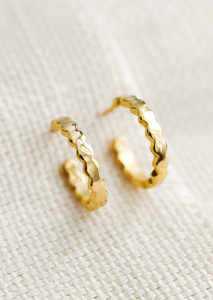 A pair of small gold hoop earrings with wavy shape.